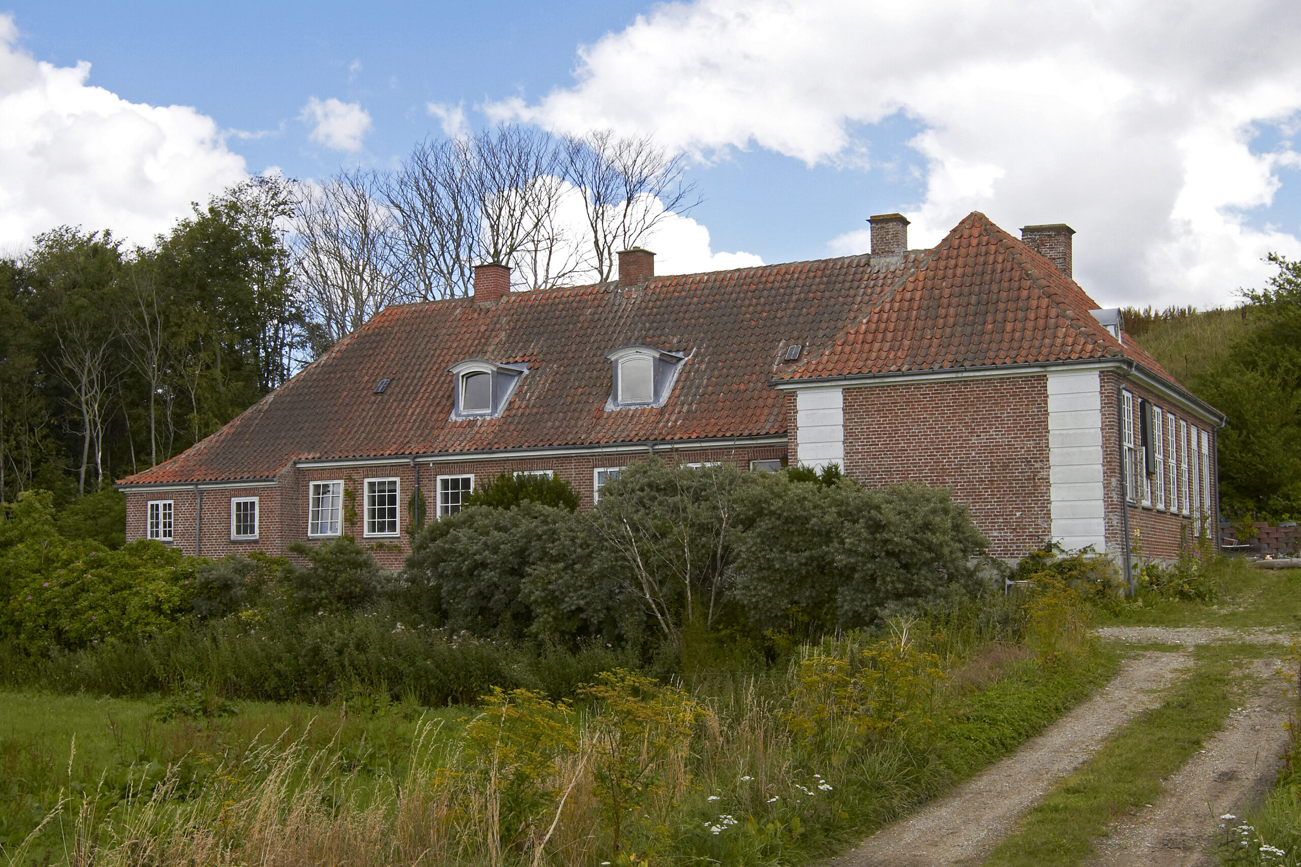Rødstens landhus med tegltag i grønne omgivelser