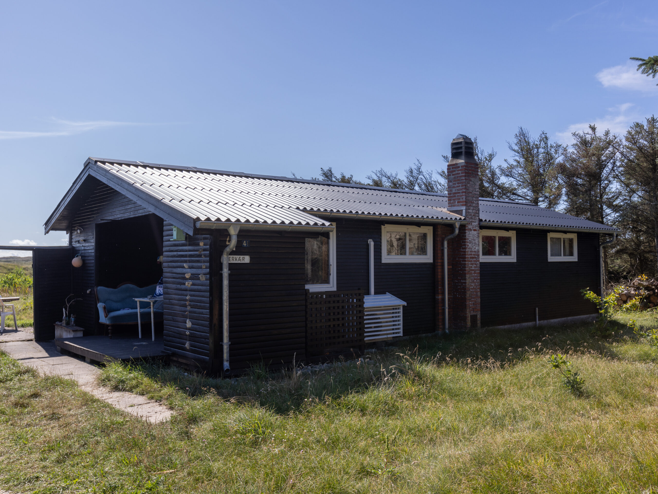 Sort sommerhus med metal tag i klitlandskab
