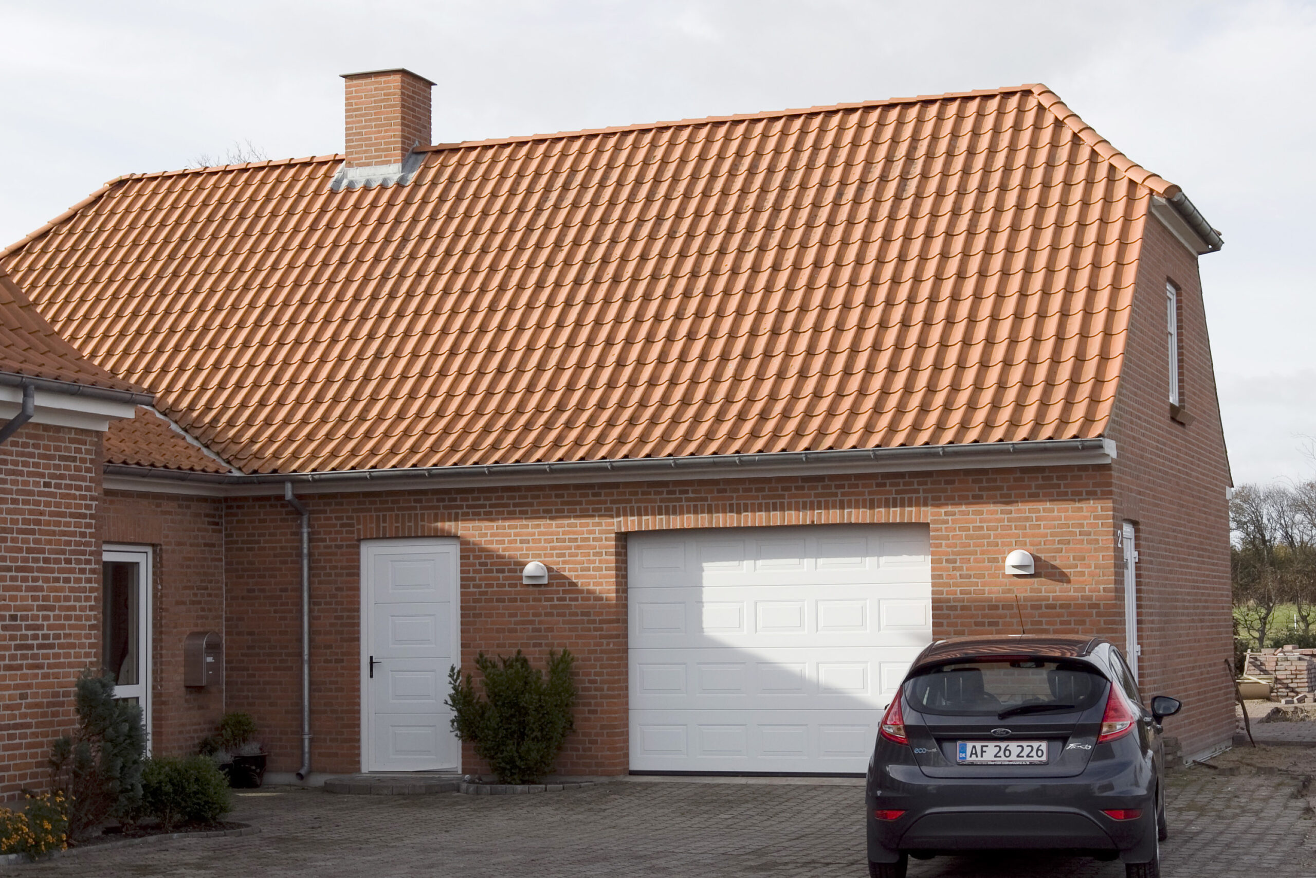 Murstenhus med rødt tegltag og garage