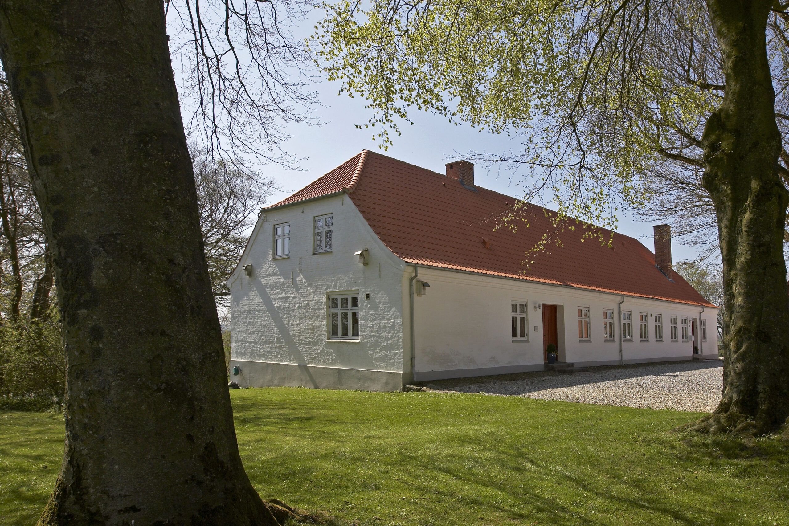 Hvidt landhus med rødt tegltag omgivet af træer