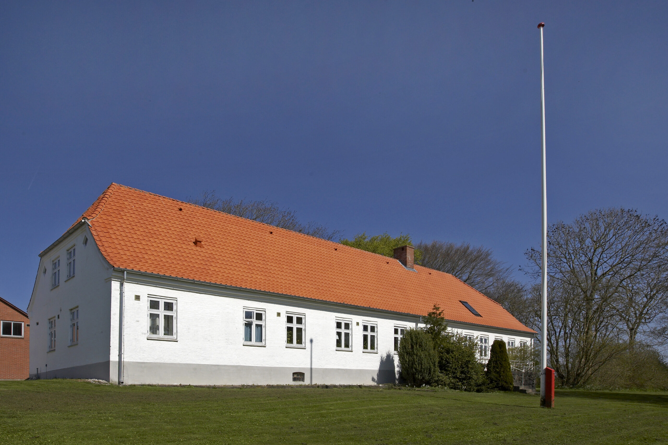 Hvidt hus med rødt tegltag og flagstang