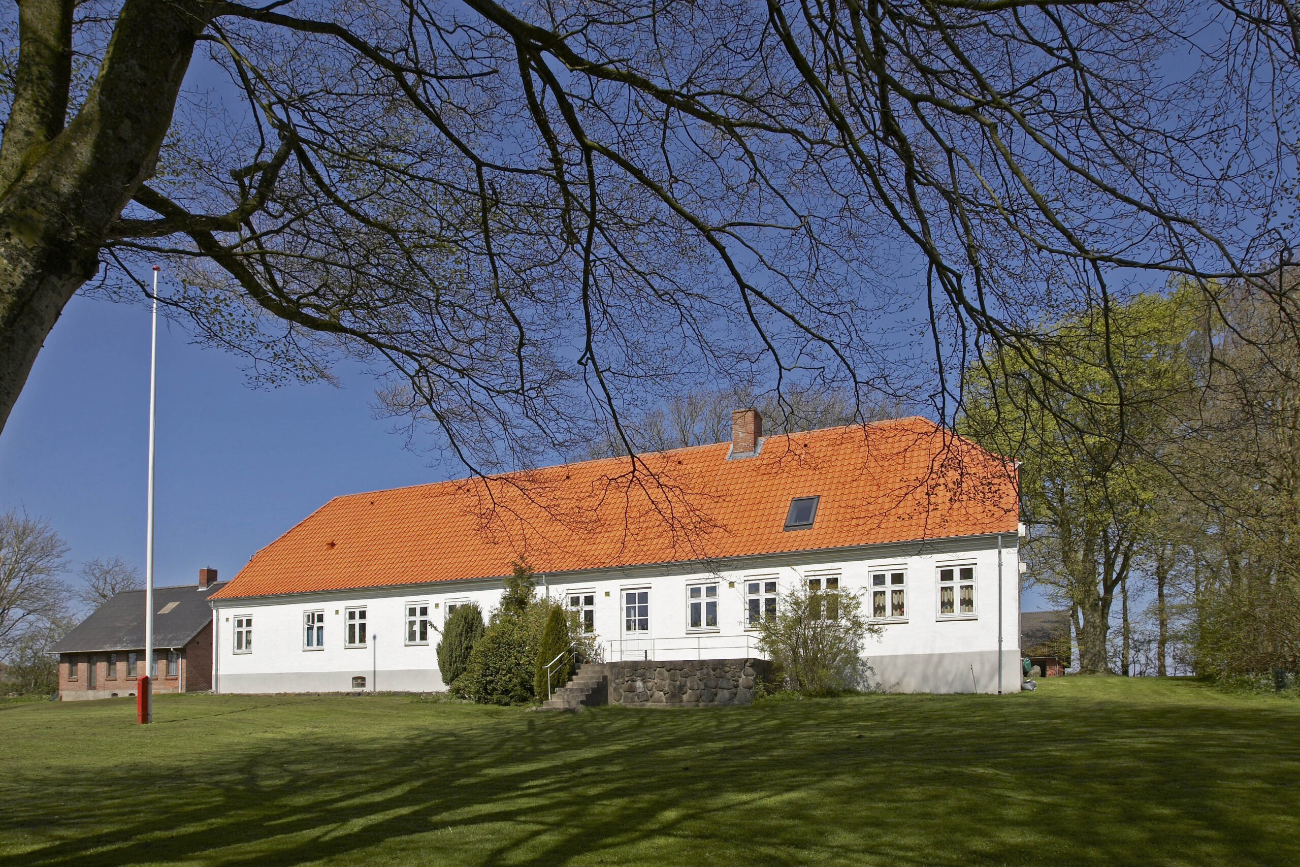 Hvidt hus med rødt tegltag og stor have