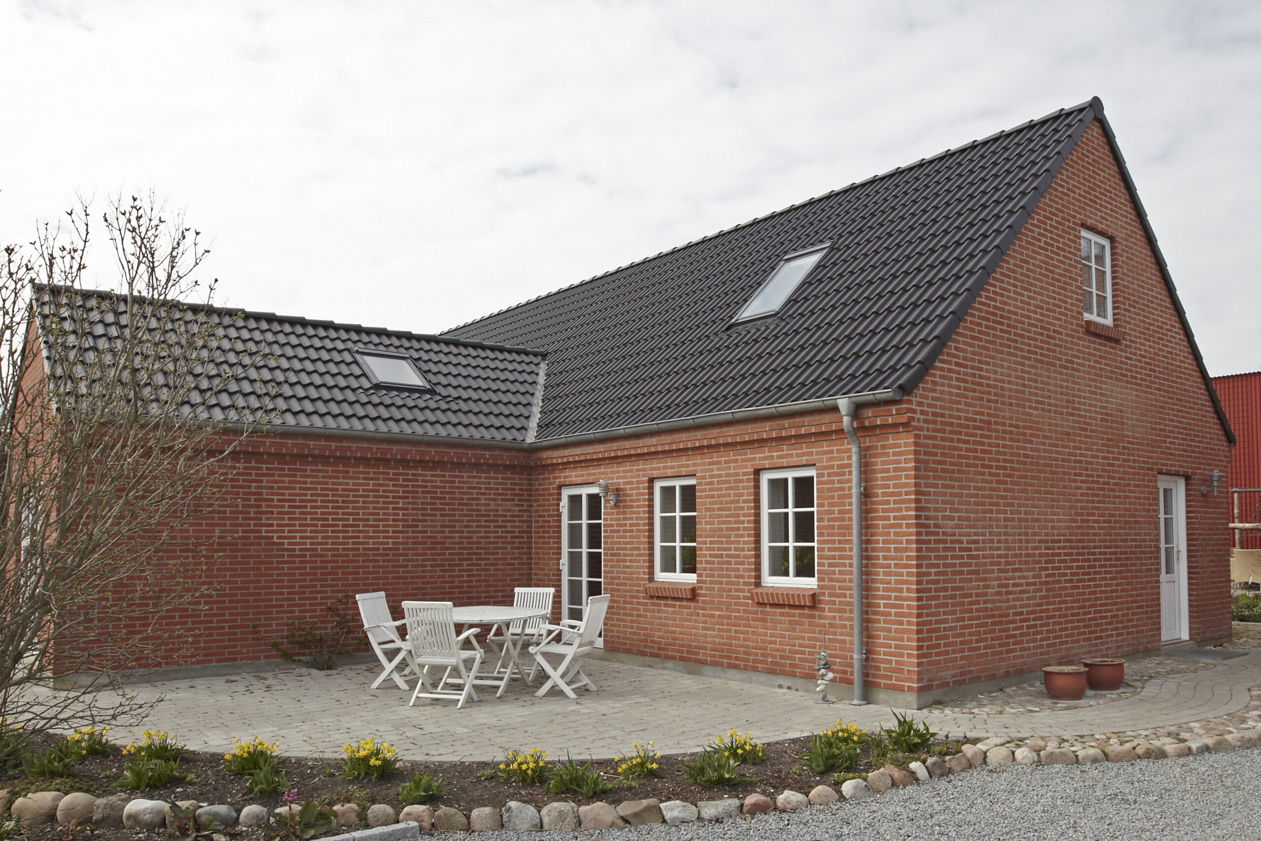 Rødstenshus med sort tegltag og terrasse