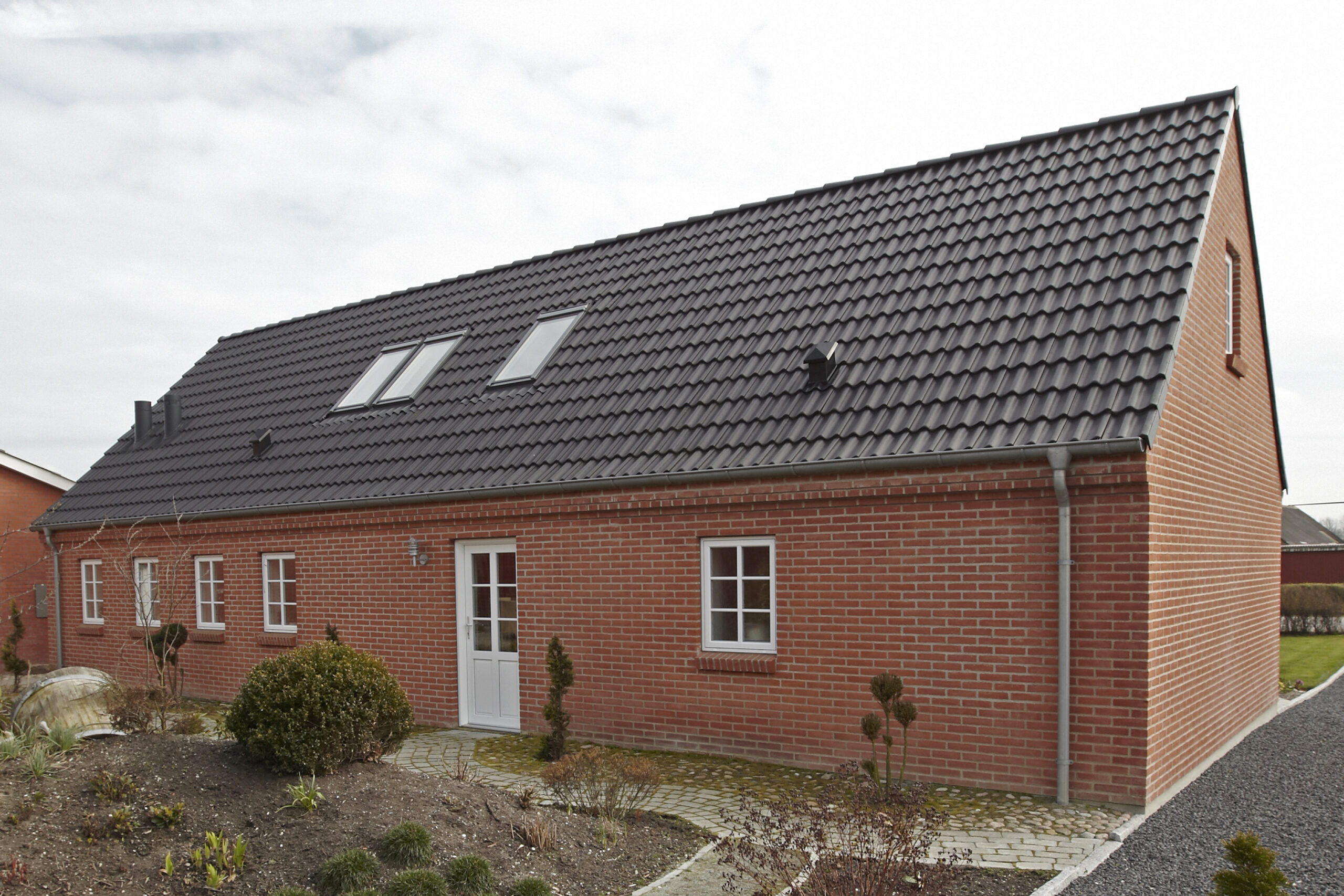 Rødstenshus med sort tegltag og ovenlysvinduer