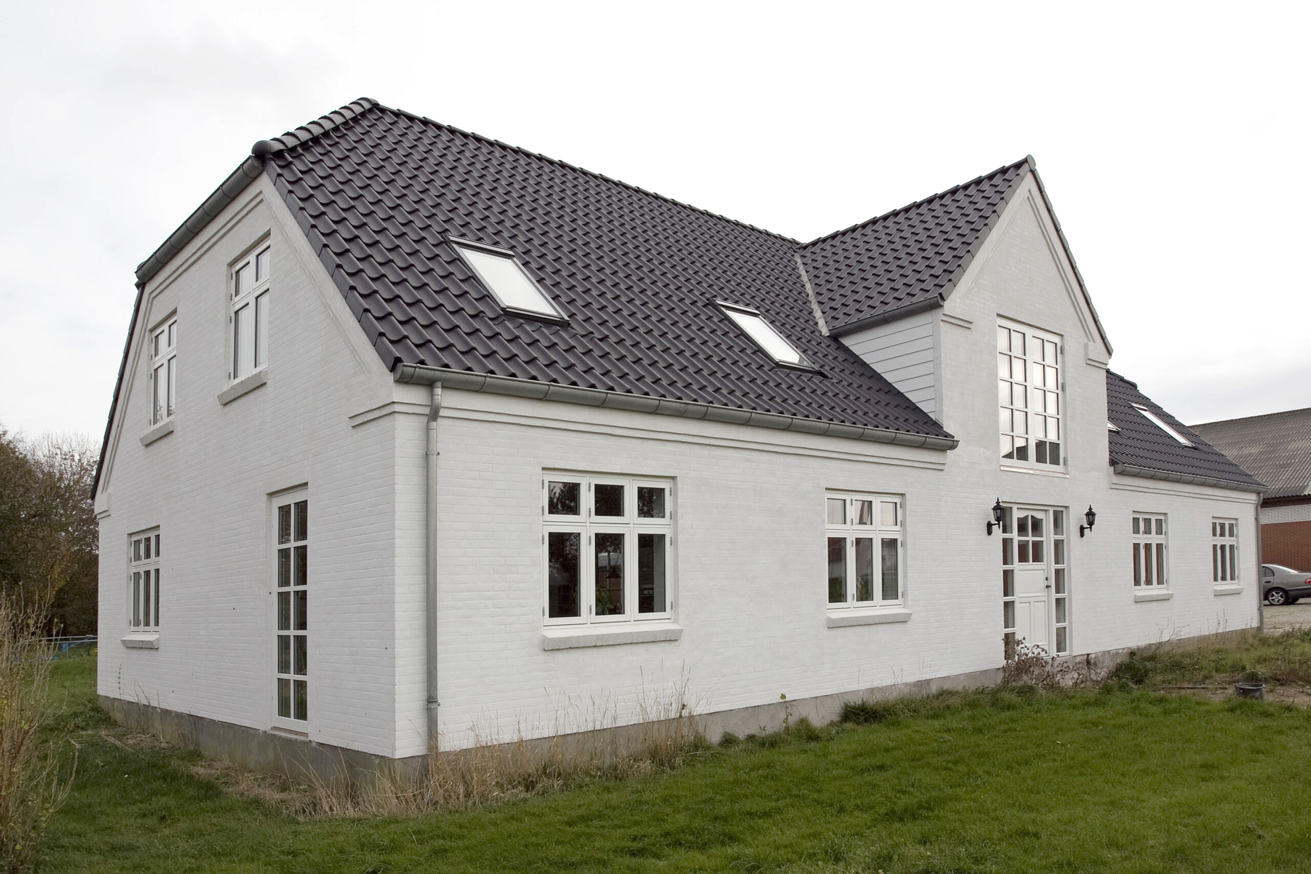 Hvid murstensvilla med mørkt tegltag og kviste