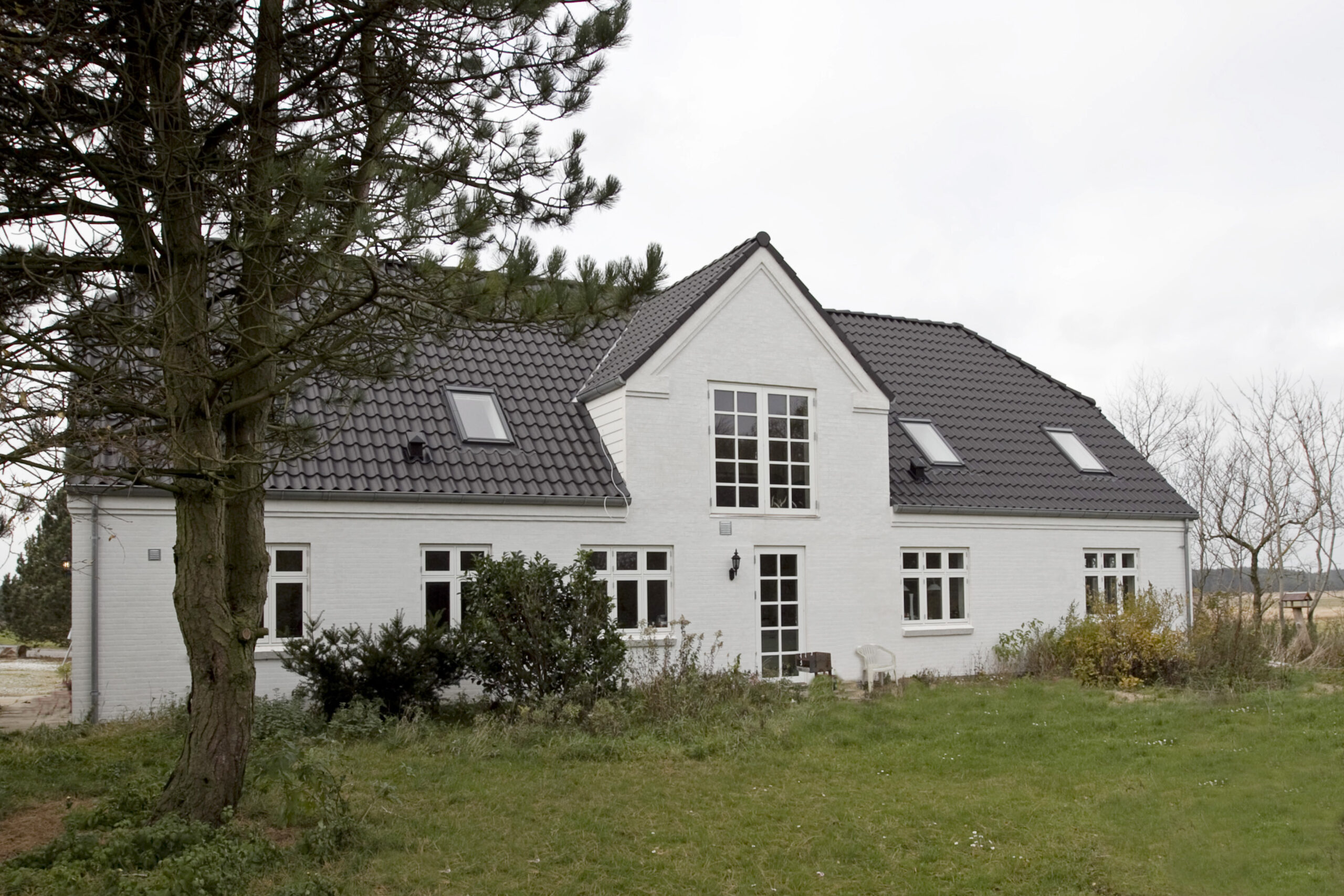Hvidt murstenshus med mørkt tegltag og have