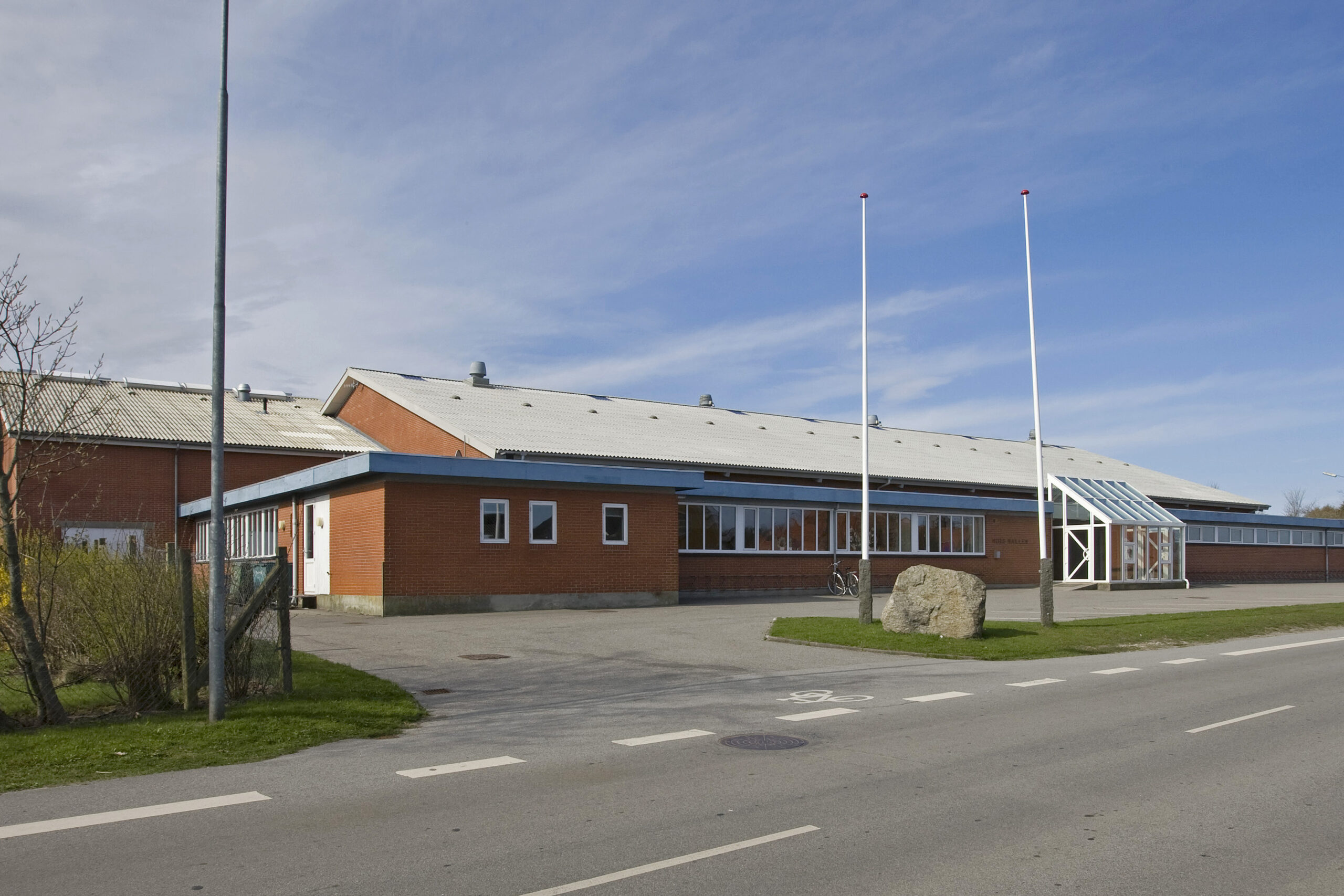 Rød murstensbygning med glasindgang og flagstænger