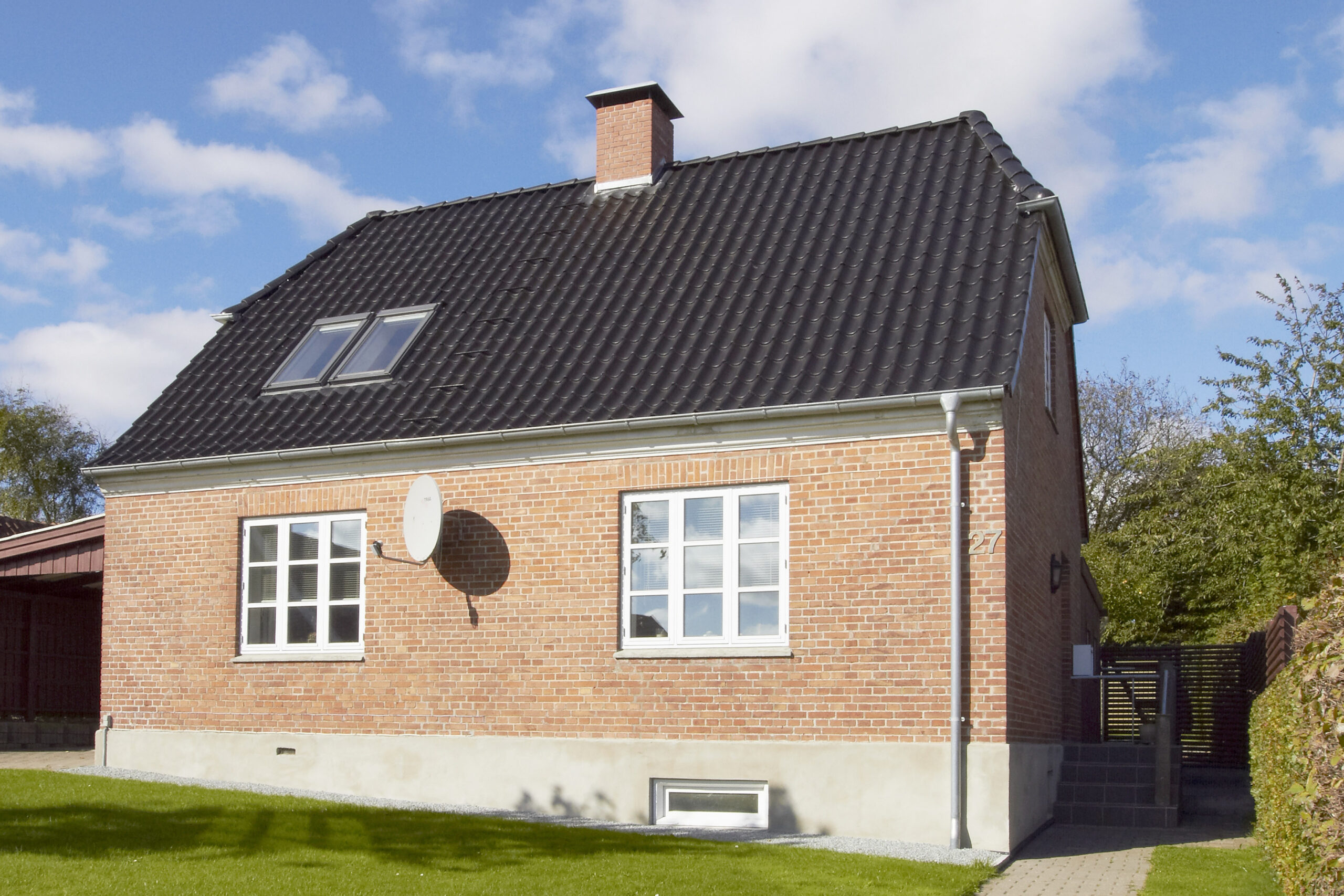 Rødstenshus med sort tegltag og ovenlysvinduer