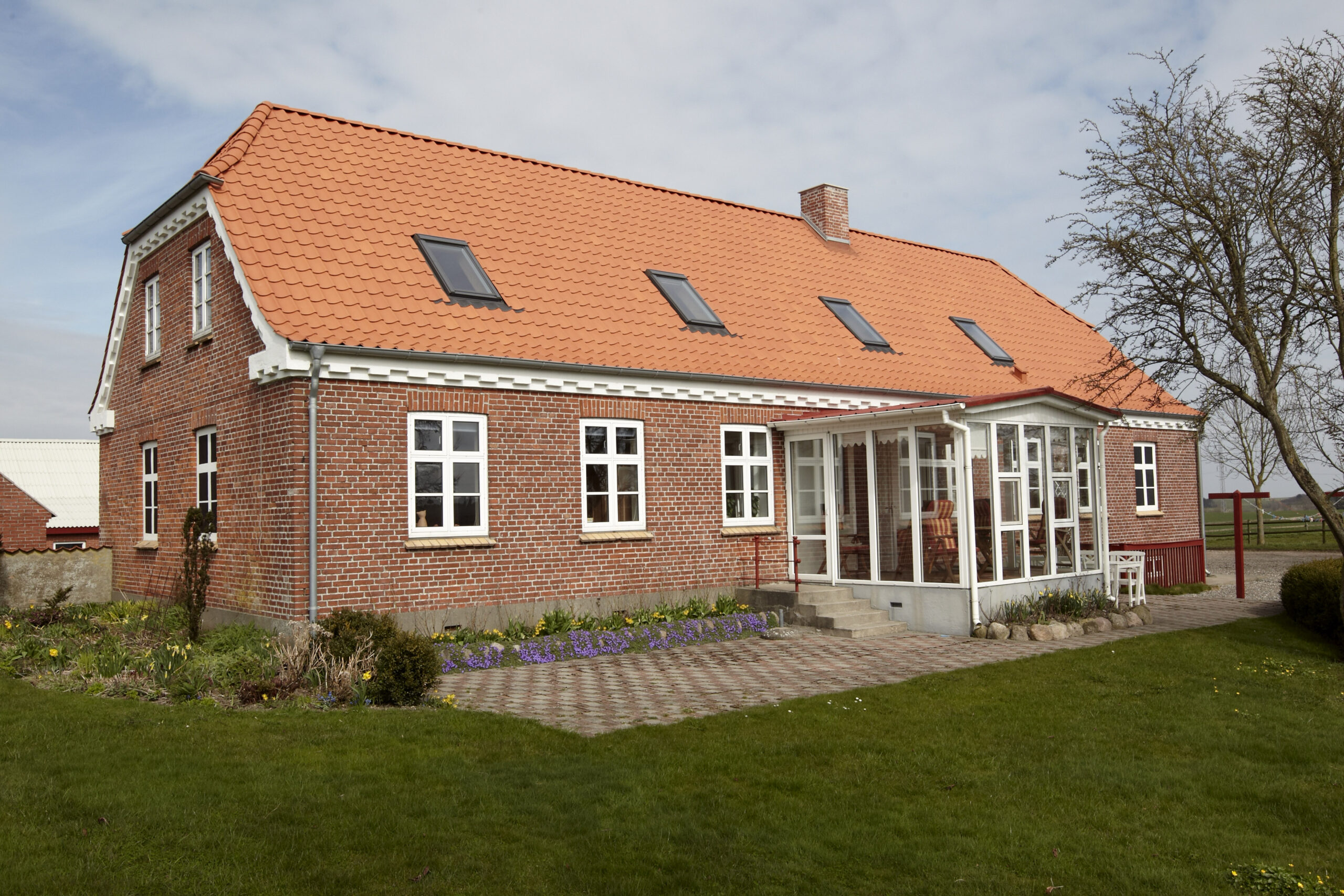 Rødstenshus med orange tegltag og udestue