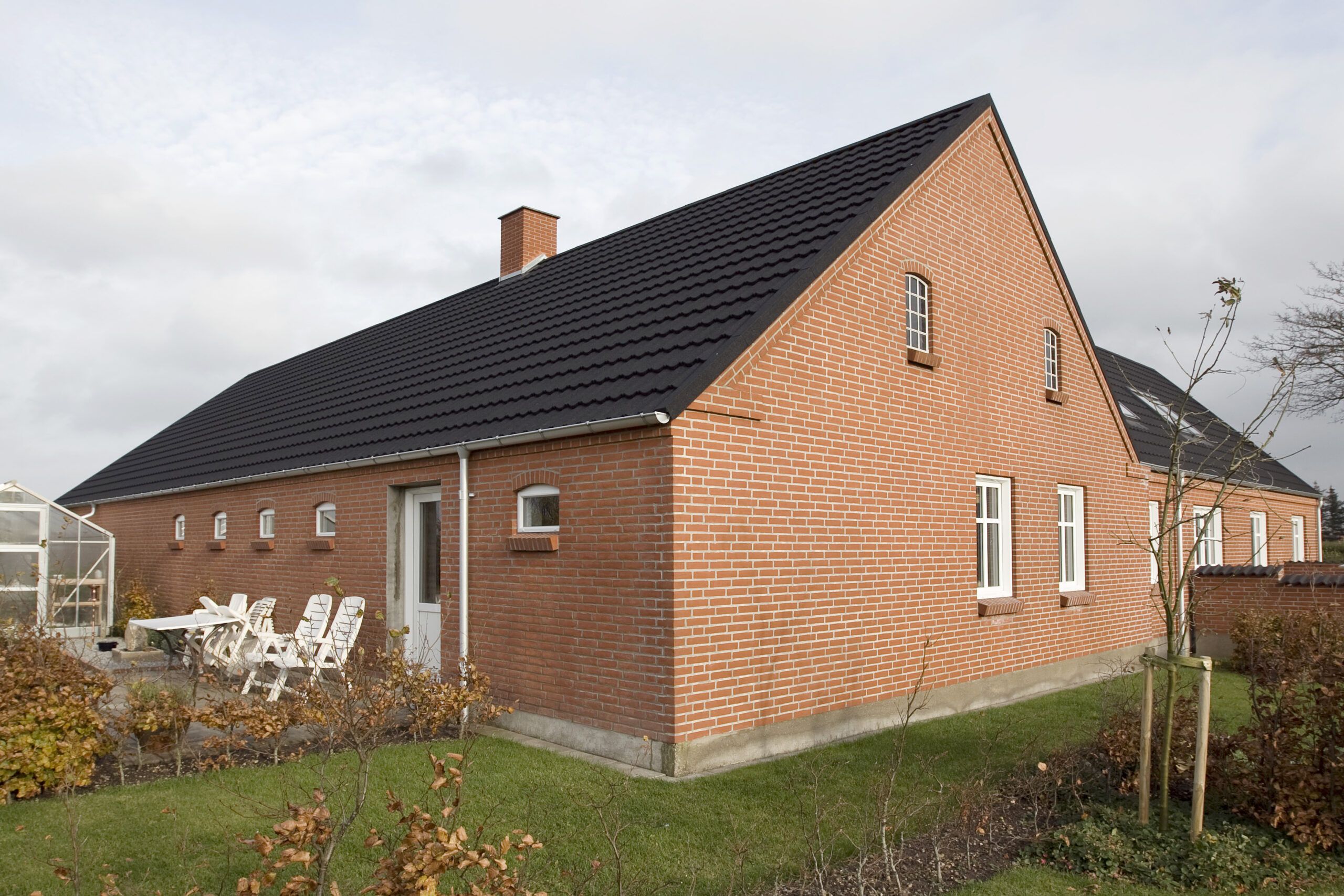 Rødstenshus med sort tegltag og have