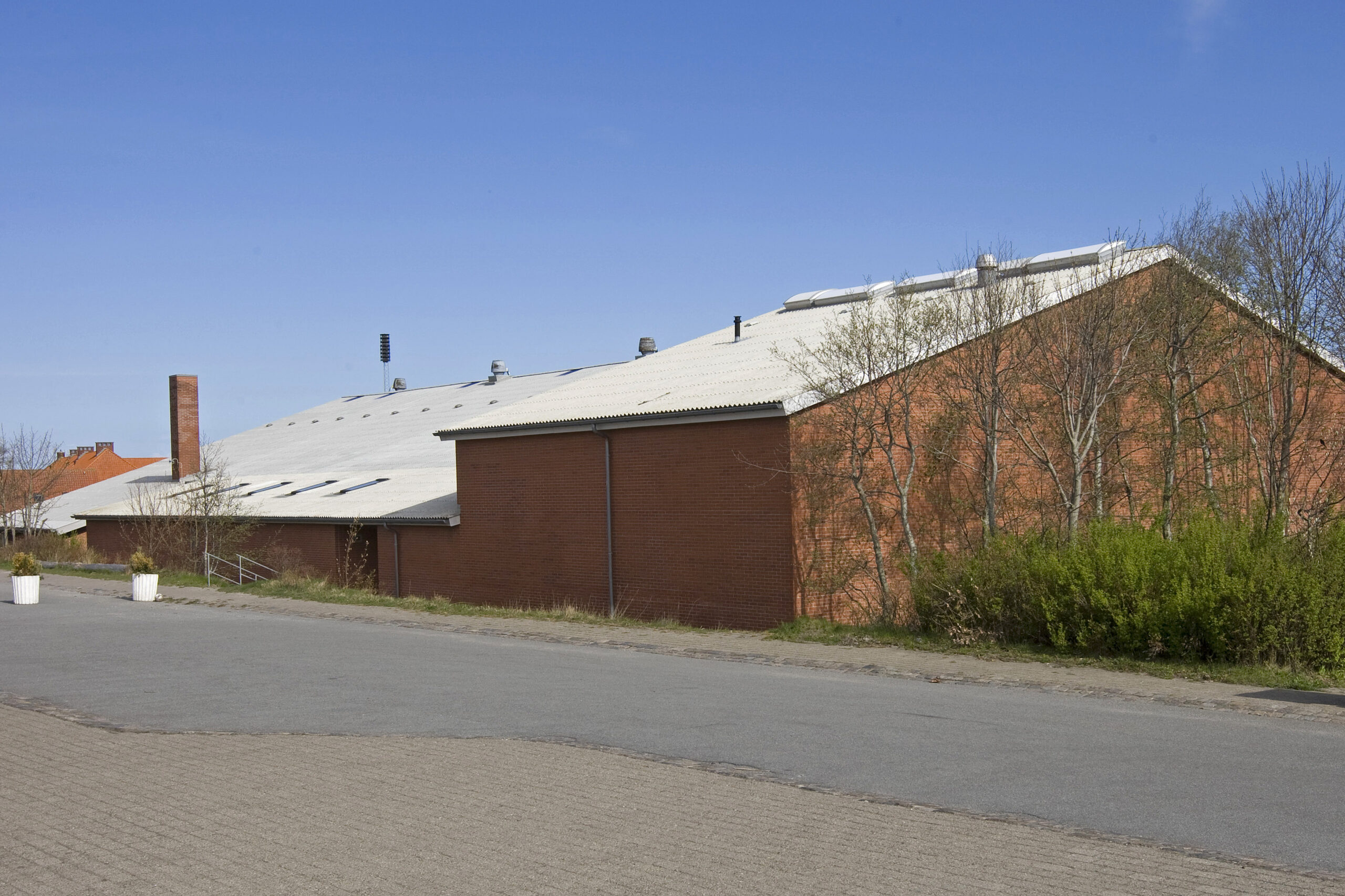 Rød murstenslagerbygning med hvidt tag ved vej