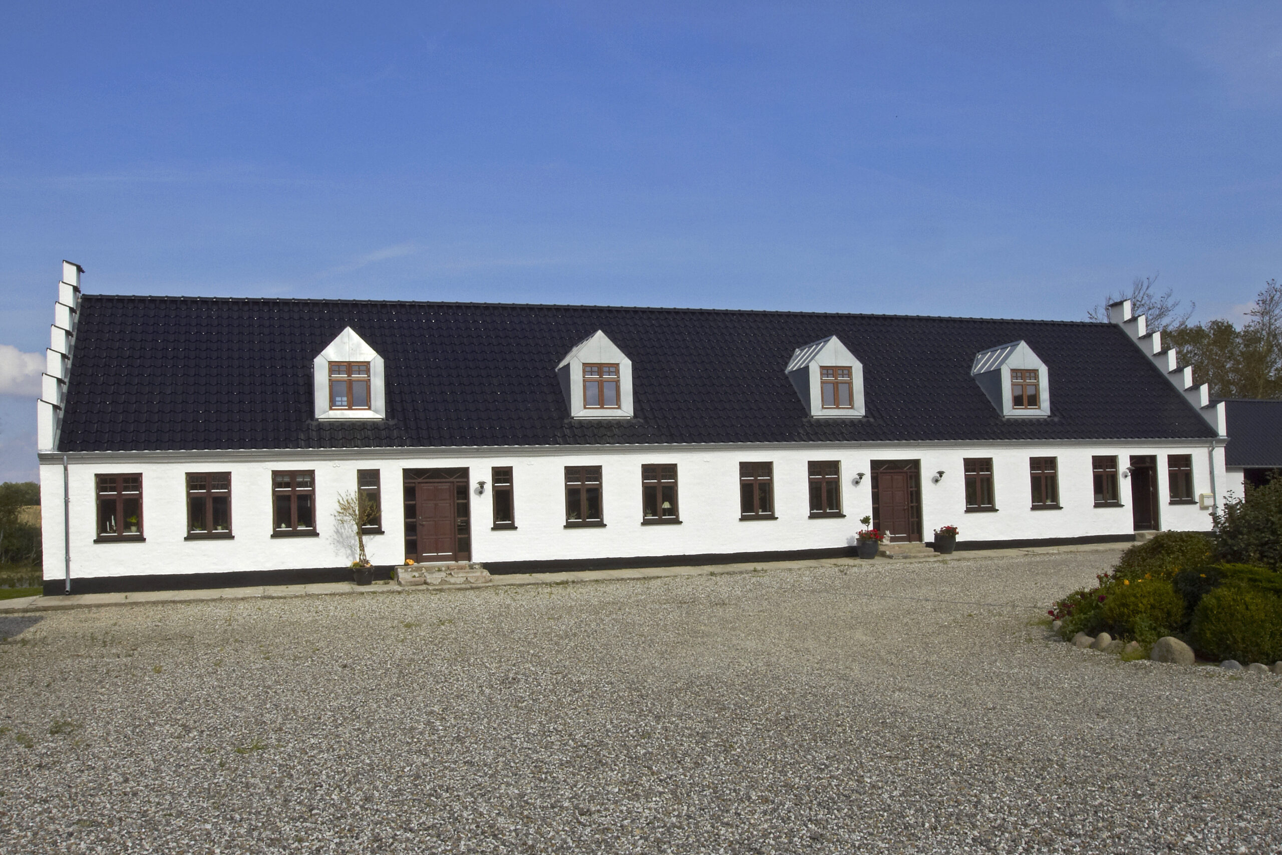 Langt hvidt landhus med sort tegltag