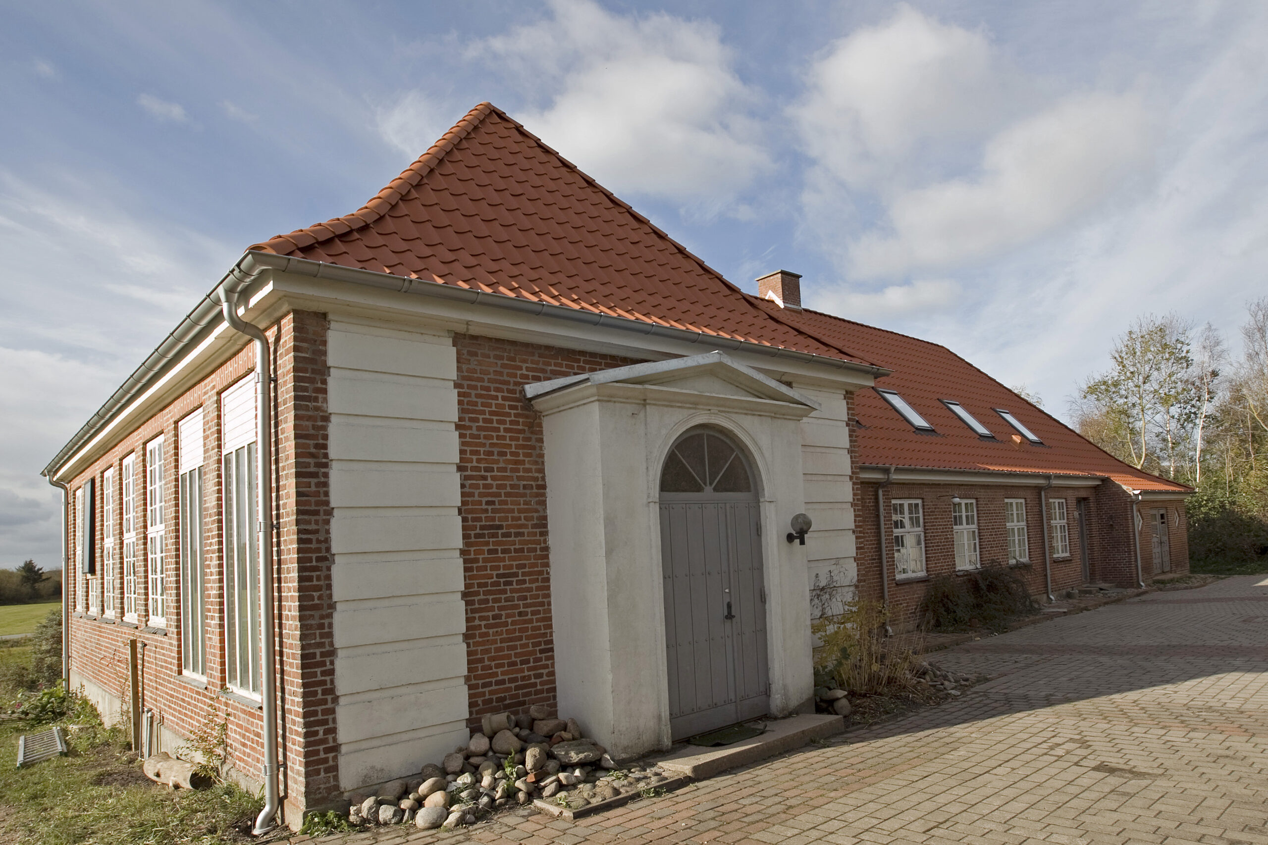 Rødstenshus med rødt tegltag og brostensindkørsel