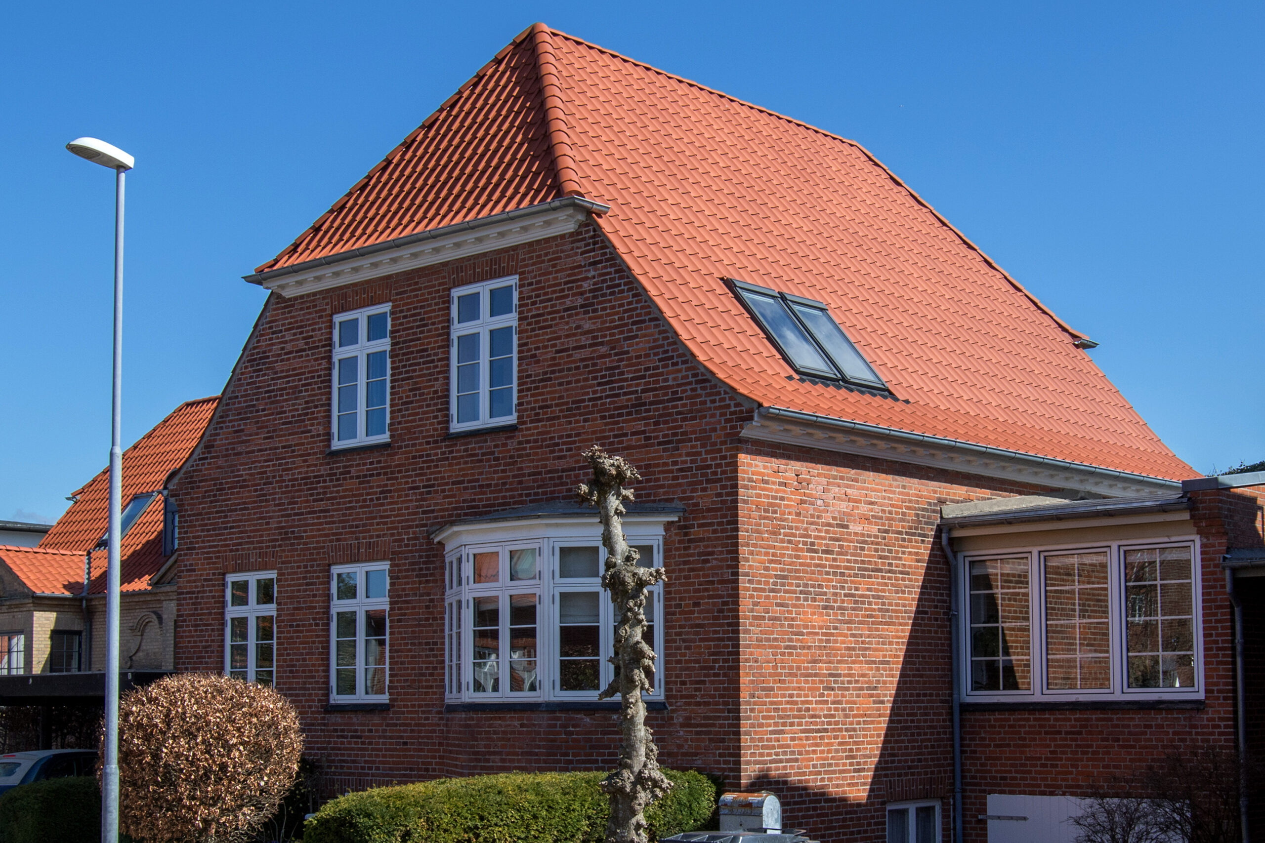 Rødstenshus med orange tegltag under blå himmel