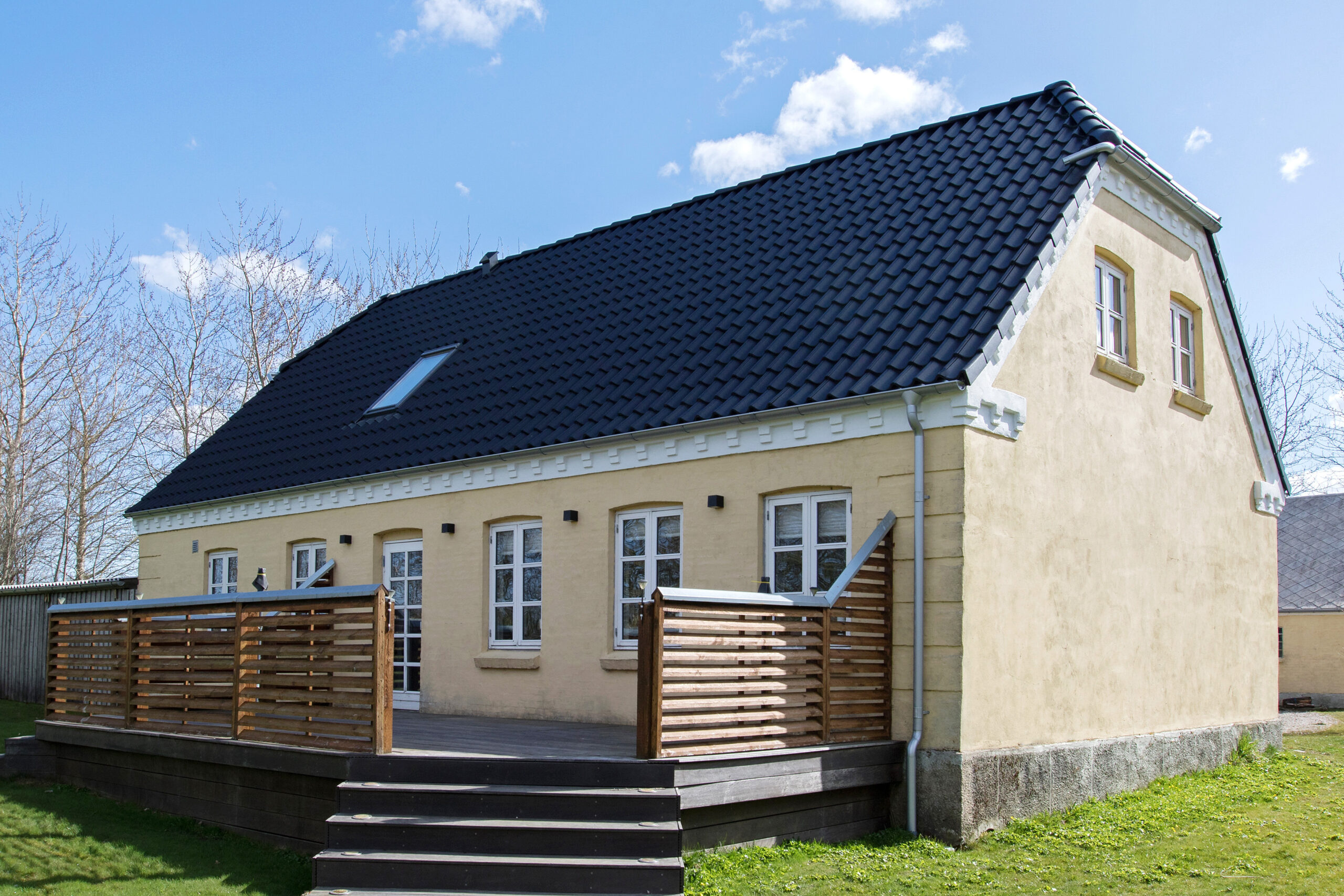 Lys gul villa med sort tegltag og terrasse