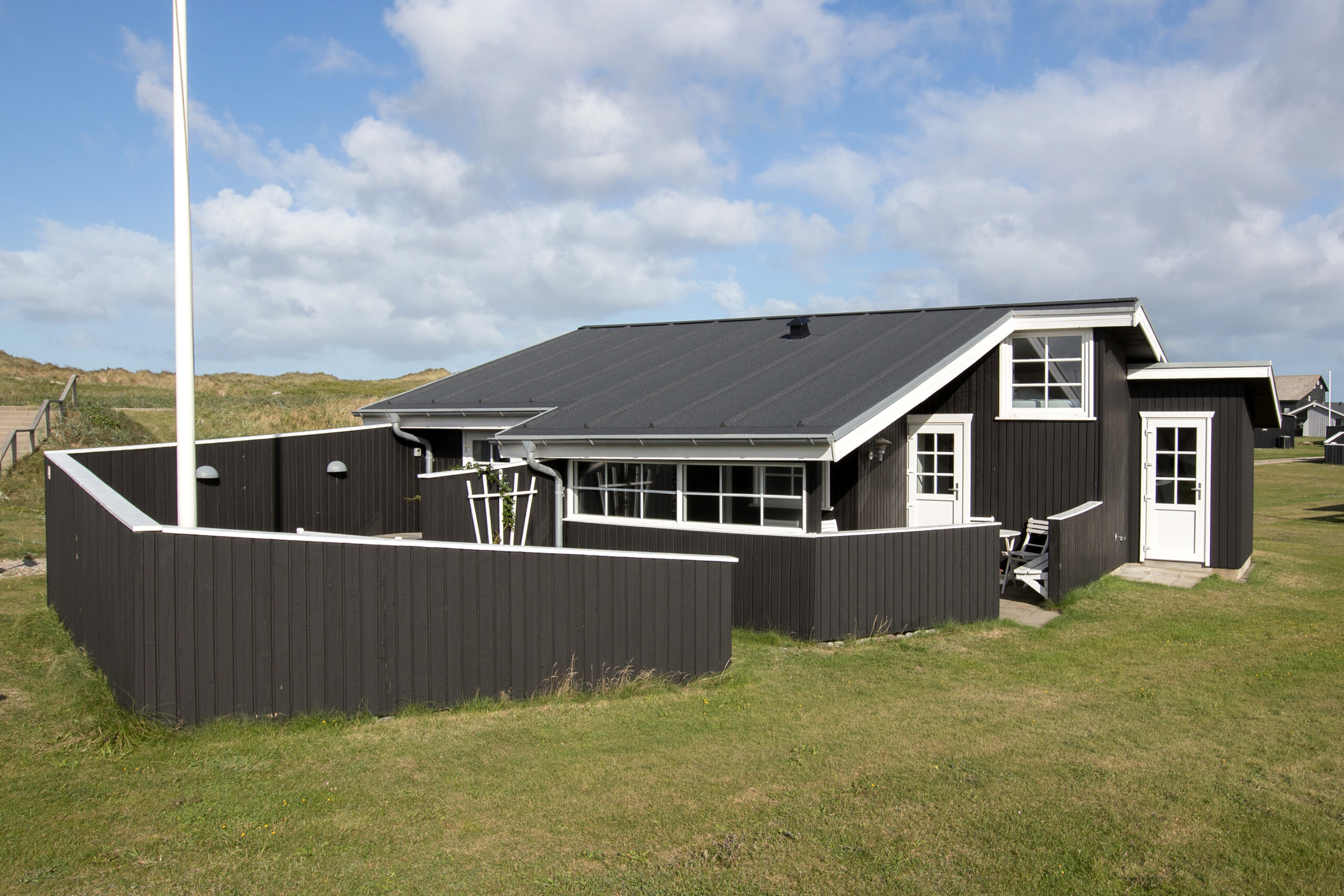Sort træsommerhus med indhegnet terrasse i klitter