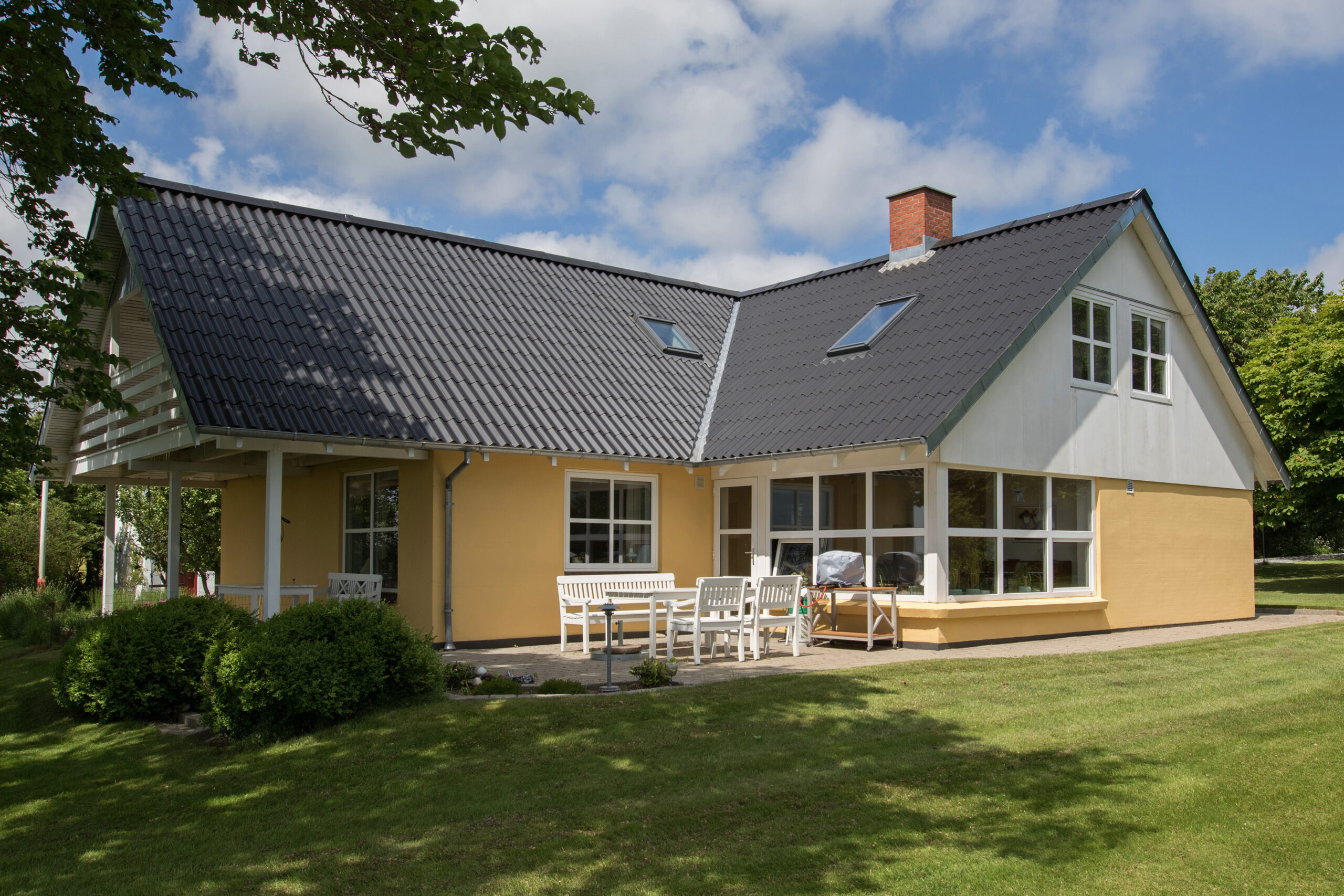 Moderne gult hus med mørkt tegltag og terrasse