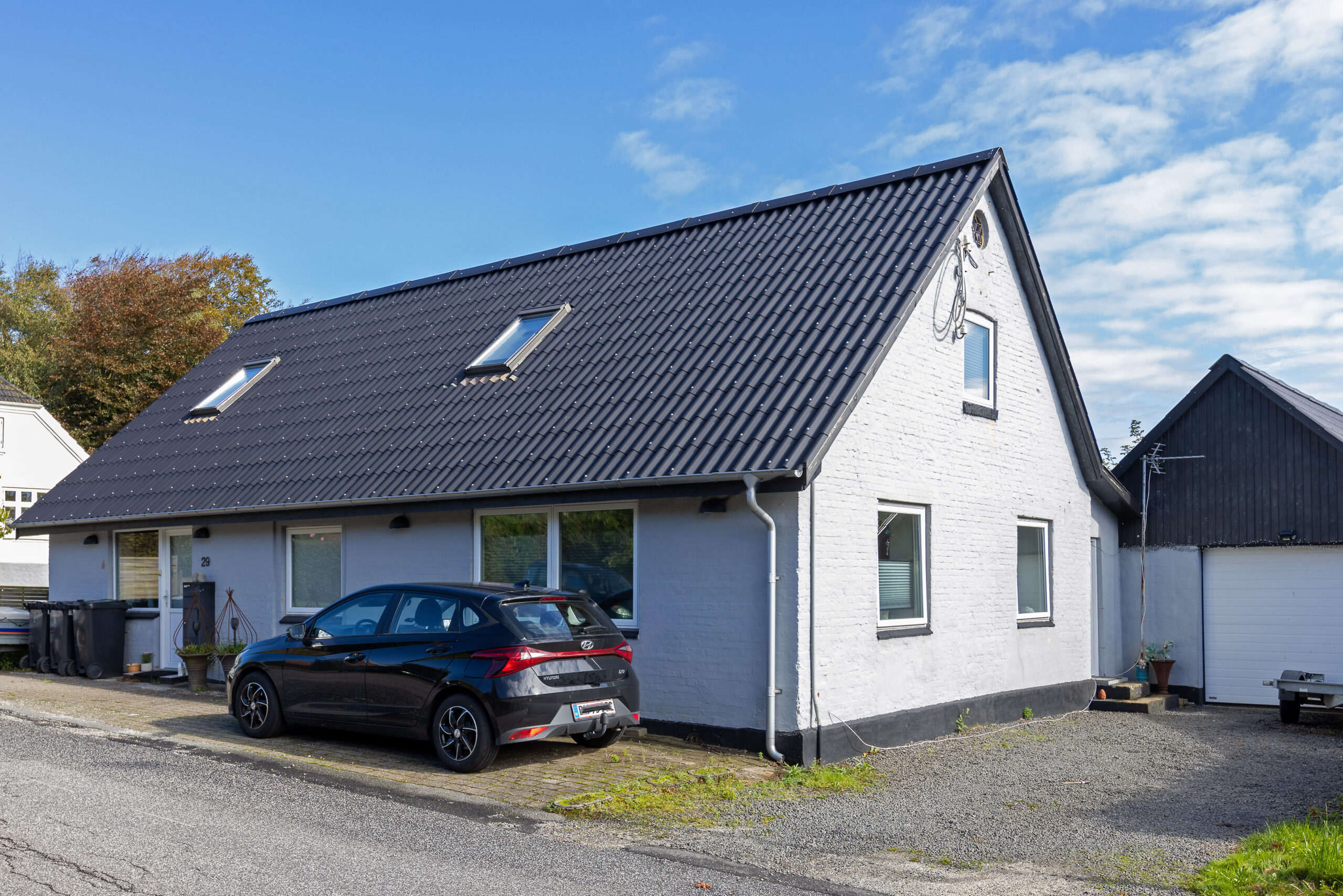 Hvidt murstenshus med sort tag og bil