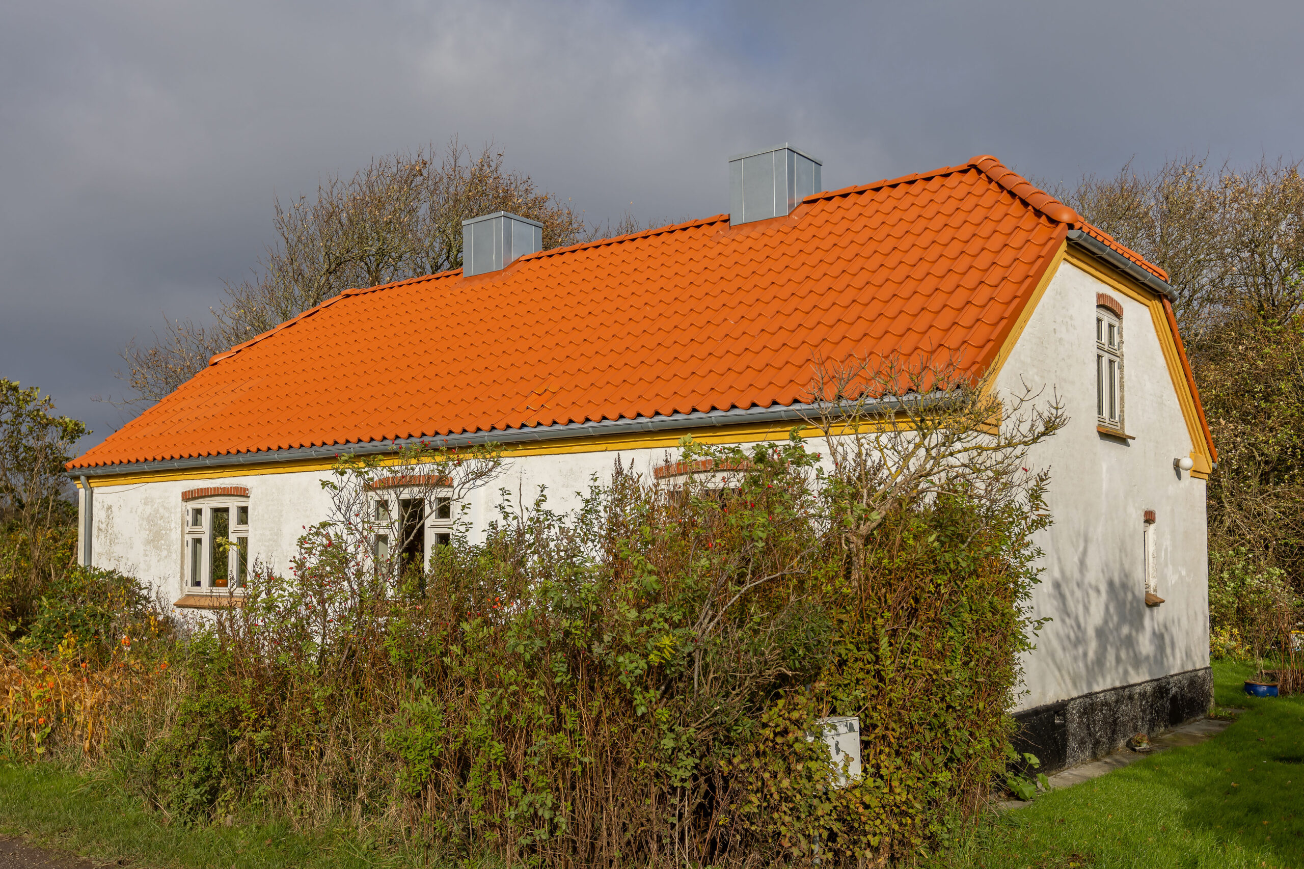Hvidt hus med orange tegltag og skorsten