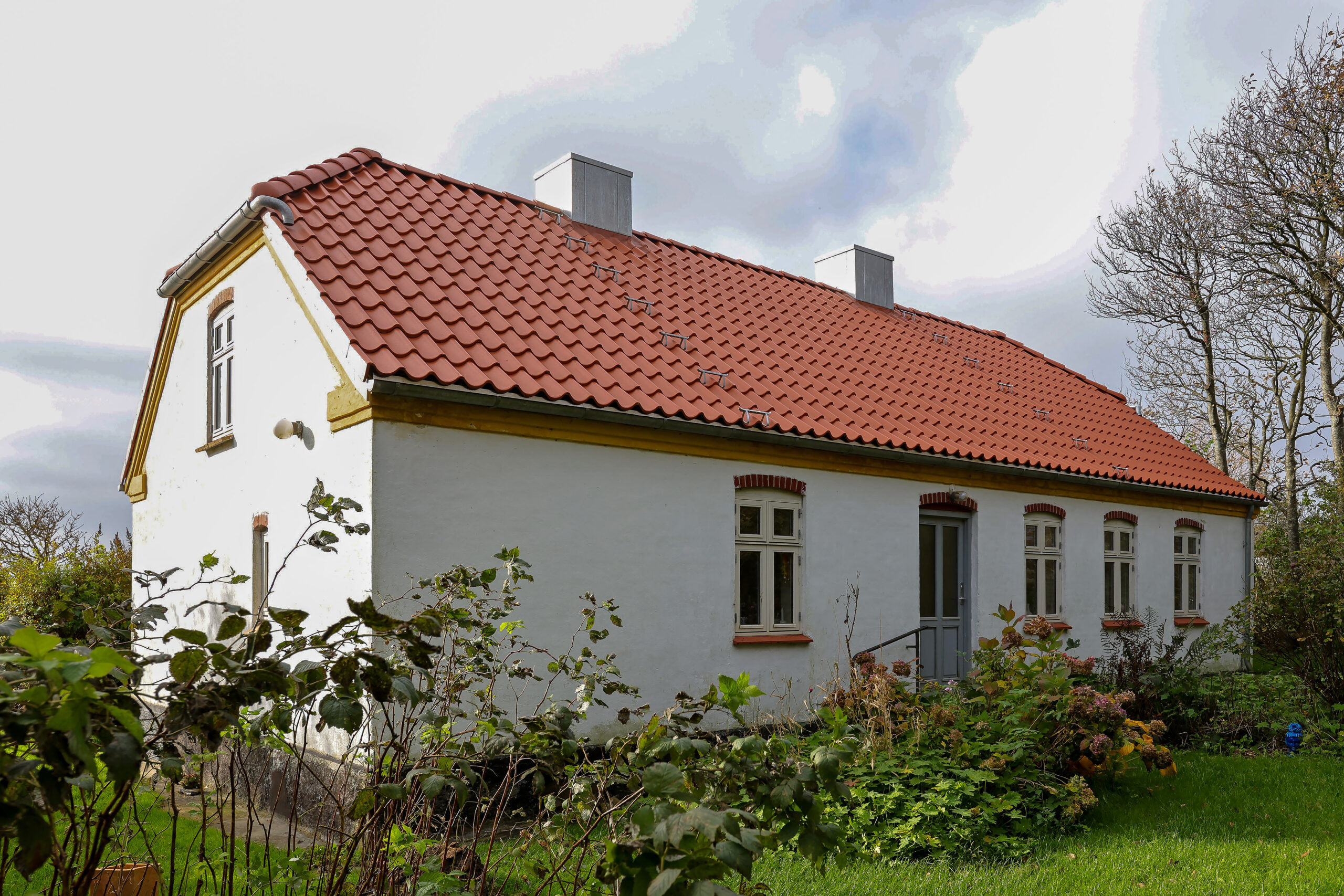 Hvidt hus med rødt tegltag og have