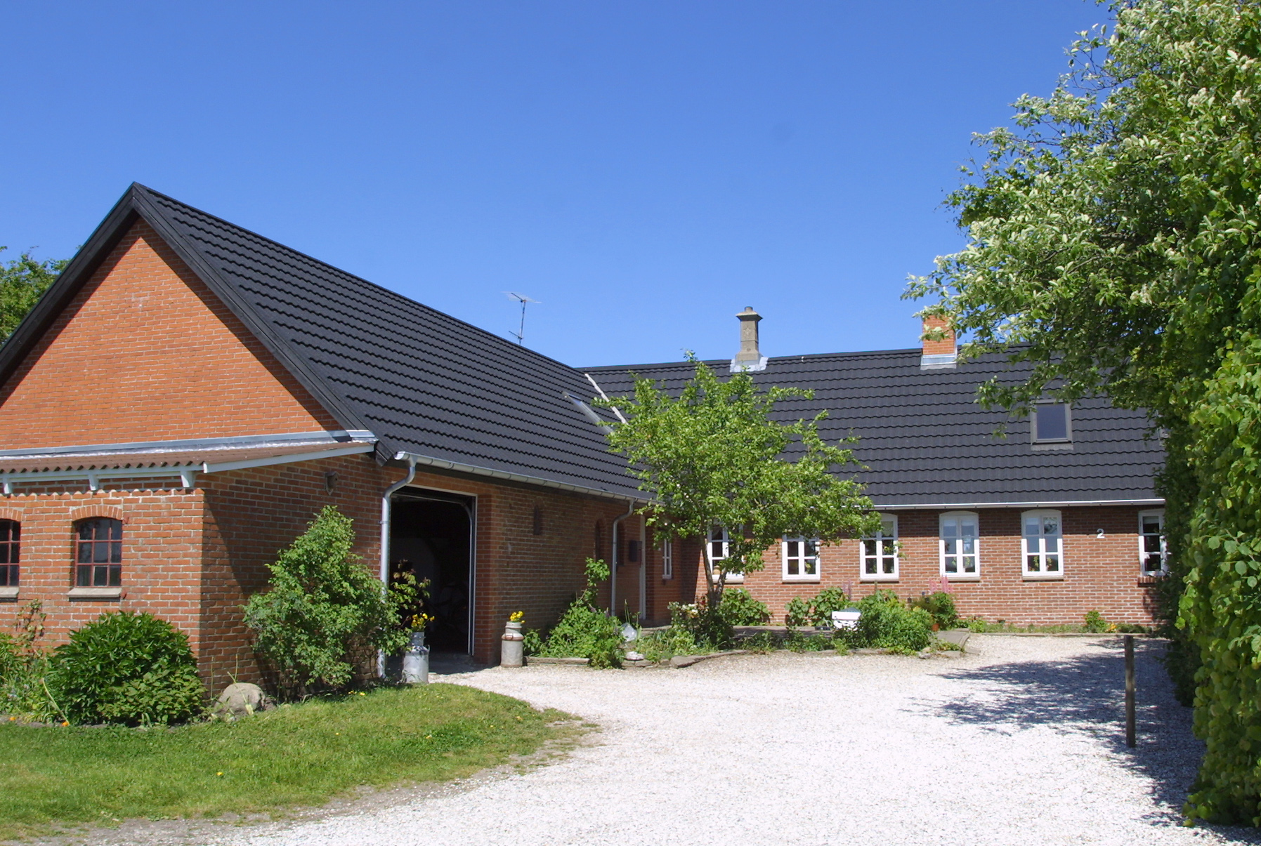 Rødstenshus med sort tag og gårdsplads