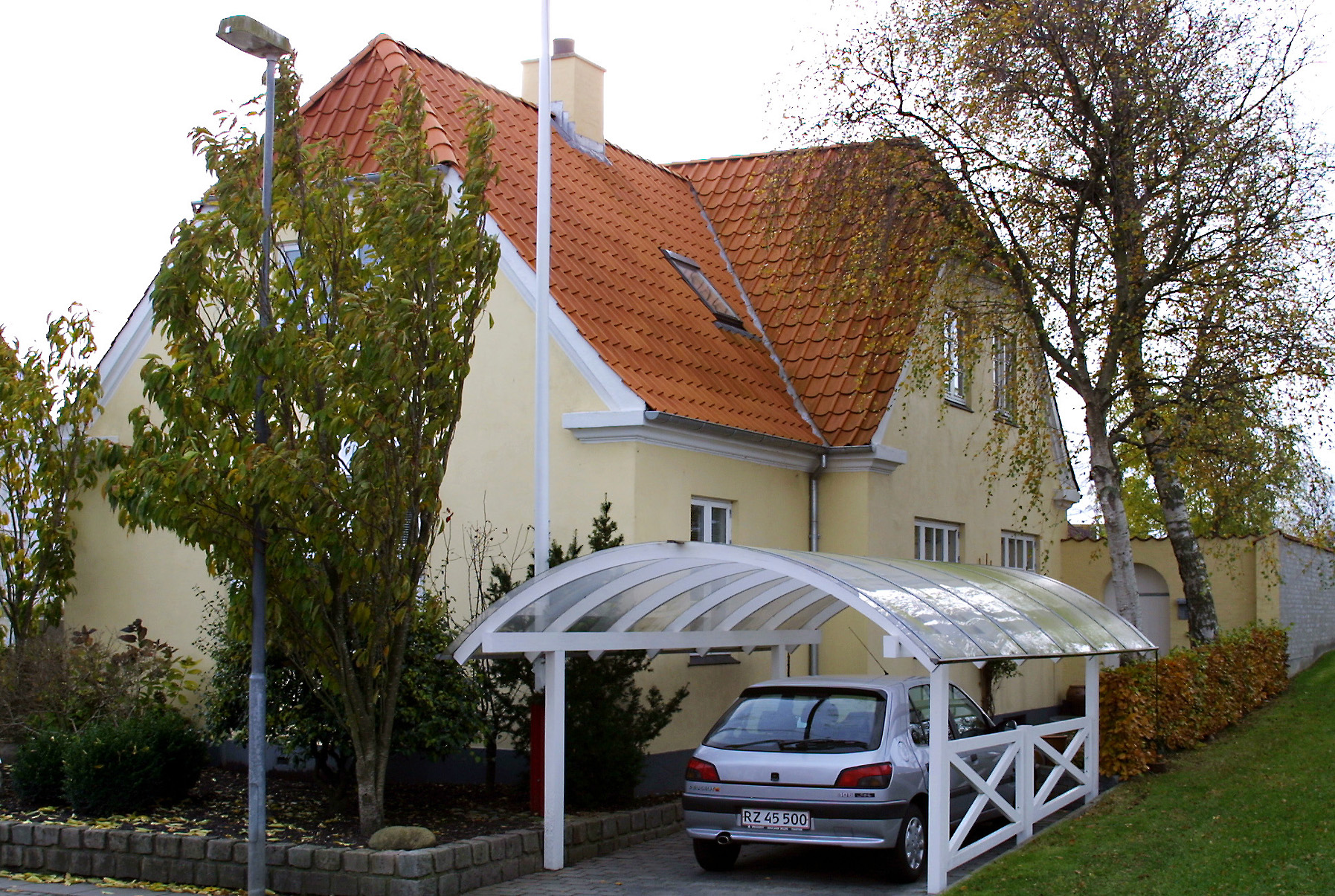 Gult hus med rødt tegltag og carport