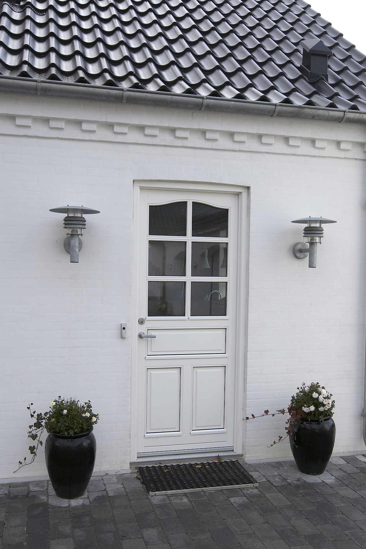 Hvid hoveddør med sorte krukker og lamper